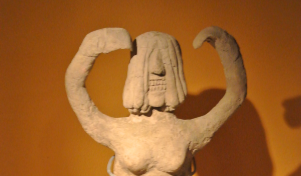 A clay figurine of an angry woman with bared teeth and arms raised.